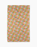 The Geometry Beachy Tile Tea Towel features an eco-friendly rectangular design with a repeating pattern of small textured squares in orange, pink, green, and pale yellow on white Geoweave fabric. Photographed with slight folds against a white background.