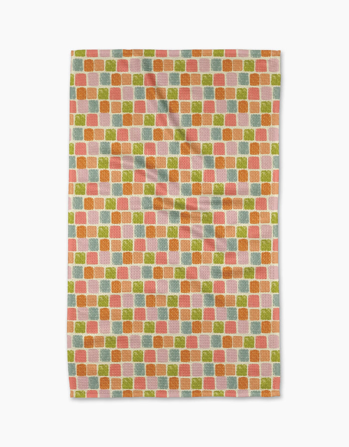 The Geometry Beachy Tile Tea Towel features an eco-friendly rectangular design with a repeating pattern of small textured squares in orange, pink, green, and pale yellow on white Geoweave fabric. Photographed with slight folds against a white background.