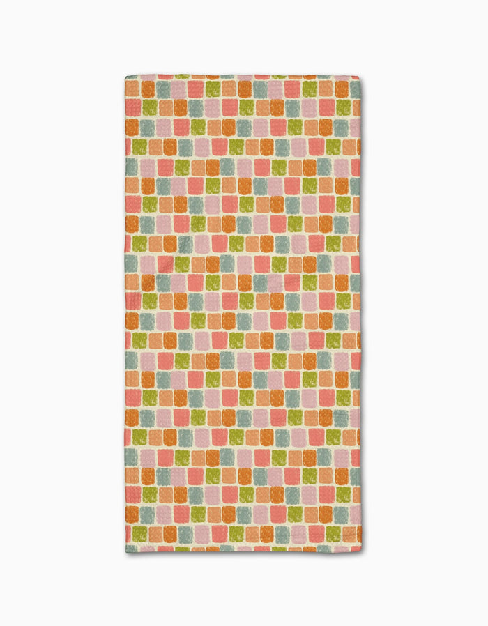 The Geometry Beachy Tile bar towel is made from Geoweave fabric and features a repeating pattern of small, colorful squares in orange, pink, green, and yellow on a light background.
