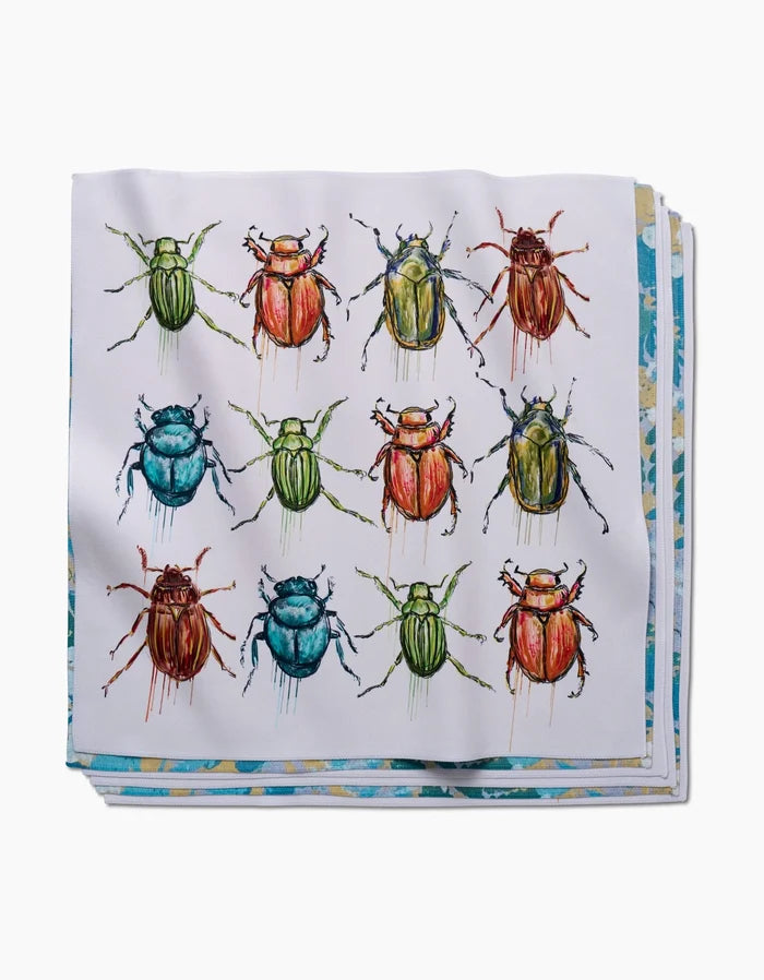 The Beetles Dinner Napkin by Taryn Brennan displays green, blue, red, and orange beetles in a grid on white eco-friendly Geosuede fabric.