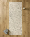 A top-down view of the GEOMETRY Bend yoga mat on a wooden floor, featuring a non-slip yoga towel and two gray blocks on the left, and a white water bottle on the right.