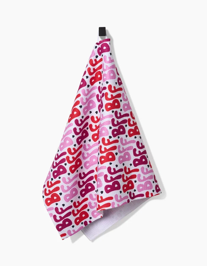 The Best Friends Forever towel by Hufton Studio features a pink, ultra-absorbent design with a repeating “BFF” pattern in red, pink, and purple, hanging from a black loop against a white background.