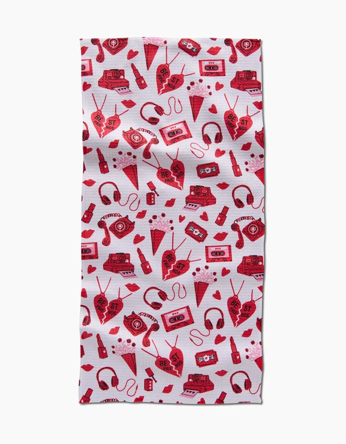 The Best Friends rectangular bar towel by Charlie Rowan Designs features a repeating red and pink pattern of hearts, cassette tapes, radios, headphones, soda bottles, and envelopes on white. Ultra-absorbent—fun and functional!.