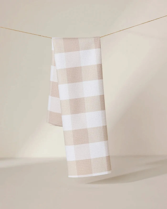 The GEOMETRY Betty Bakes eco-friendly kitchen towel in beige and white checkered design hangs neatly over a thin clothesline, set against a softly lit neutral background.