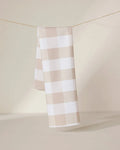 The GEOMETRY Betty Bakes eco-friendly kitchen towel in beige and white checkered design hangs neatly over a thin clothesline, set against a softly lit neutral background.