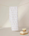 A light beige and white floral-patterned GEOMETRY tea towel, Bettys Buds, hangs on a string against a neutral background. In the foreground, an ultra-absorbent dish brush and a bar of soap rest on a dish.