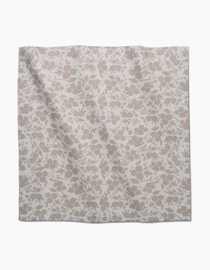 The GEOMETRY Bettys Buds napkin is a square cloth made from recycled Geosuede, showcasing a light beige floral pattern with assorted flowers and leaves on a white background.