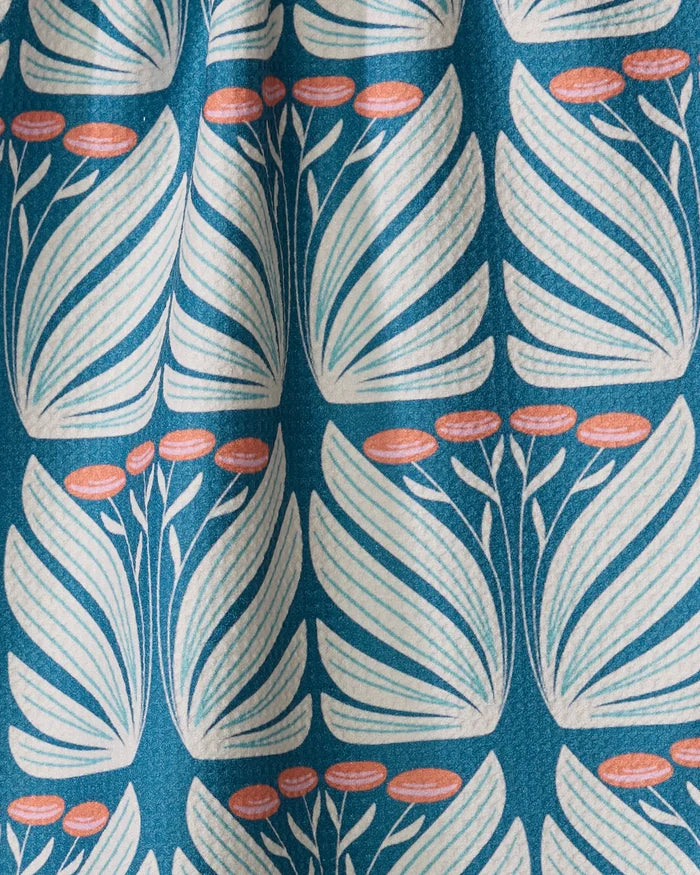Beyond the Gate by Rebecca Woolbright is a retro botanical tea towel in blue, featuring white stylized leaves and small orange oval flowers. It’s made from quick-drying recycled material and softly gathered for an elegant look.