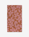 The GEOMETRY Big Fuchsia Flowers rectangular cloth napkin showcases large pink blossoms and leaves on a burnt orange background, displayed flat on white, and crafted with ultra-absorbent Geoweave technology for enhanced function.