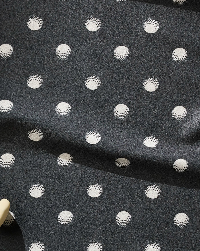 The Geometry Birdie towel features dark gray recycled fabric with a repeating pattern of solid and outlined white polka dots. Ultra-absorbent and slightly shiny, it's perfect for fitness use and shows visible folds in its design.