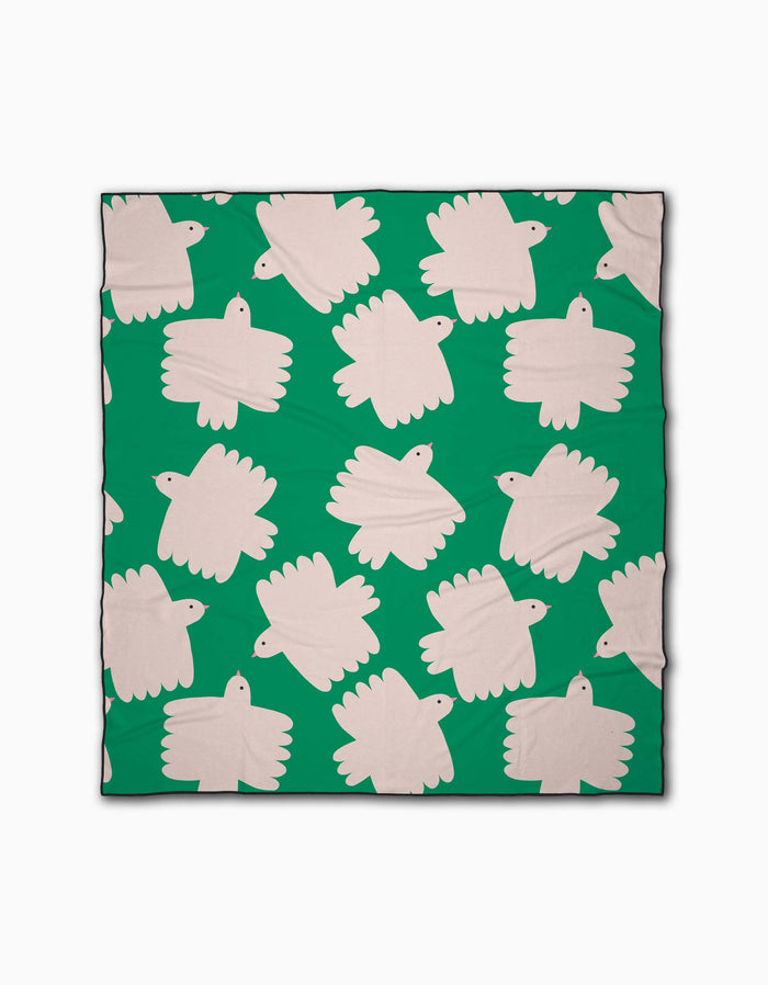 The Birds beach blanket by Jennifer Bouron is green, made from recycled materials, and displays stylized white birds in a repeating, minimal pattern across its quick-drying surface.