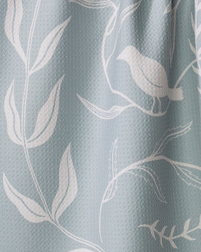 Birdsong by Elana Gabrielle is an eco-friendly, light blue textured kitchen towel with a minimalist white botanical and bird pattern featuring branches, leaves, and a perched bird.