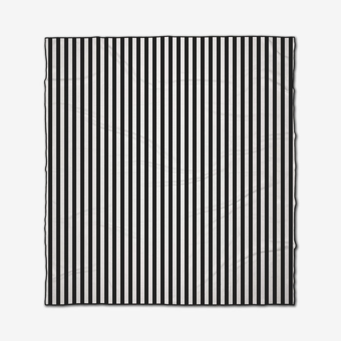 The GEOMETRY Black Stripes is a square recycled beach blanket with evenly spaced vertical black and white stripes, slightly wrinkled and shown against a white background.