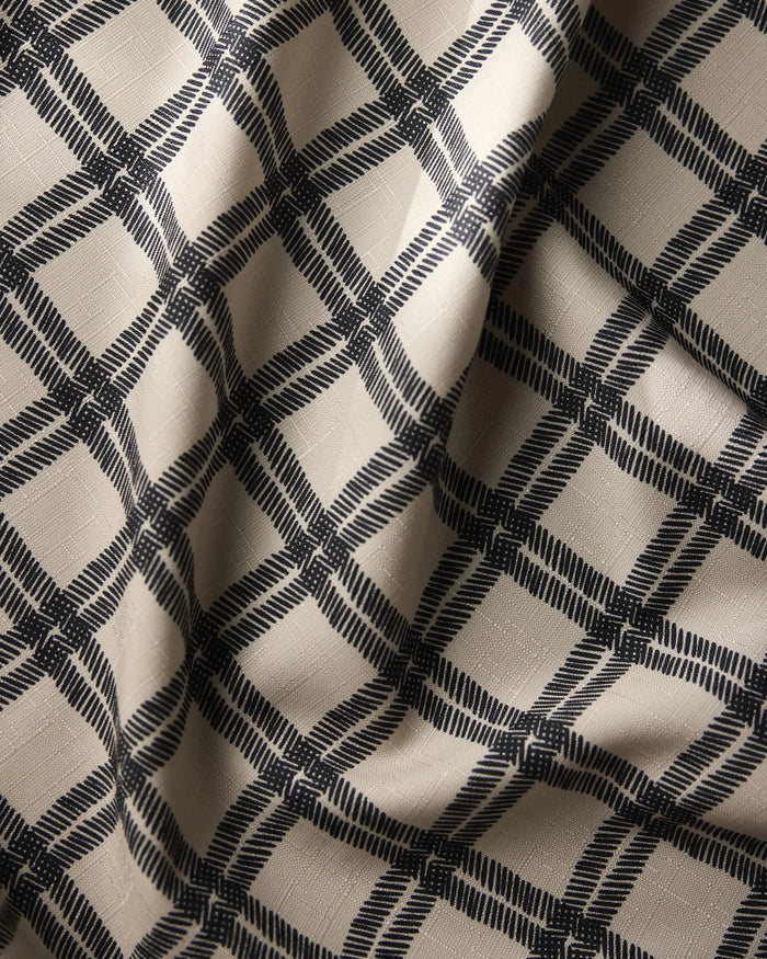 The Geometry Blackstone table runner shows a close-up of beige fabric with a dark navy blue plaid pattern and visible light creases, adding subtle shadows and texture.