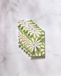 Six "Bliss and Bloom" greeting cards by GEOMETRY, featuring white daisies and green leaves, are arranged in a neat overlapping row on a marble surface. Crafted from eco-friendly paper towels for a sustainable touch.
