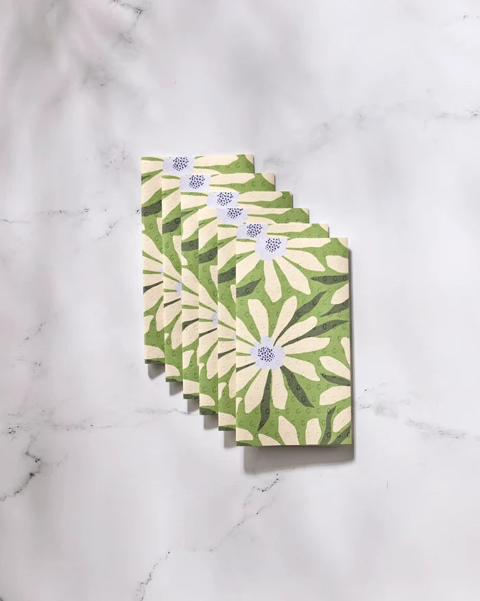 Six "Bliss and Bloom" greeting cards by GEOMETRY, featuring white daisies and green leaves, are arranged in a neat overlapping row on a marble surface. Crafted from eco-friendly paper towels for a sustainable touch.