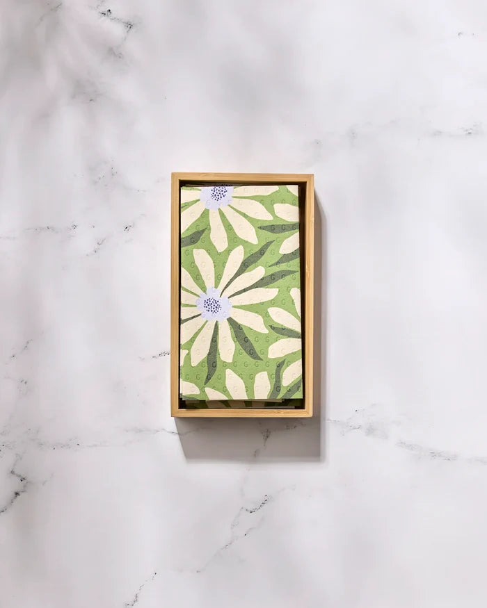 The Bliss and Bloom tray by GEOMETRY features a green background with white daisy-like flowers and purple centers, styled with eco-friendly paper towels on a white marble surface.
