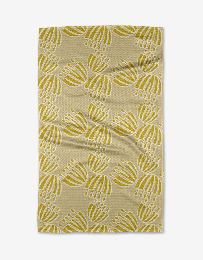 The Block Print Tulips tea towel by Lizzie Clark features a beige background with a repeating yellow and white abstract floral pattern, crafted from Geoweave fabric and shown laid flat with slight wrinkles visible.