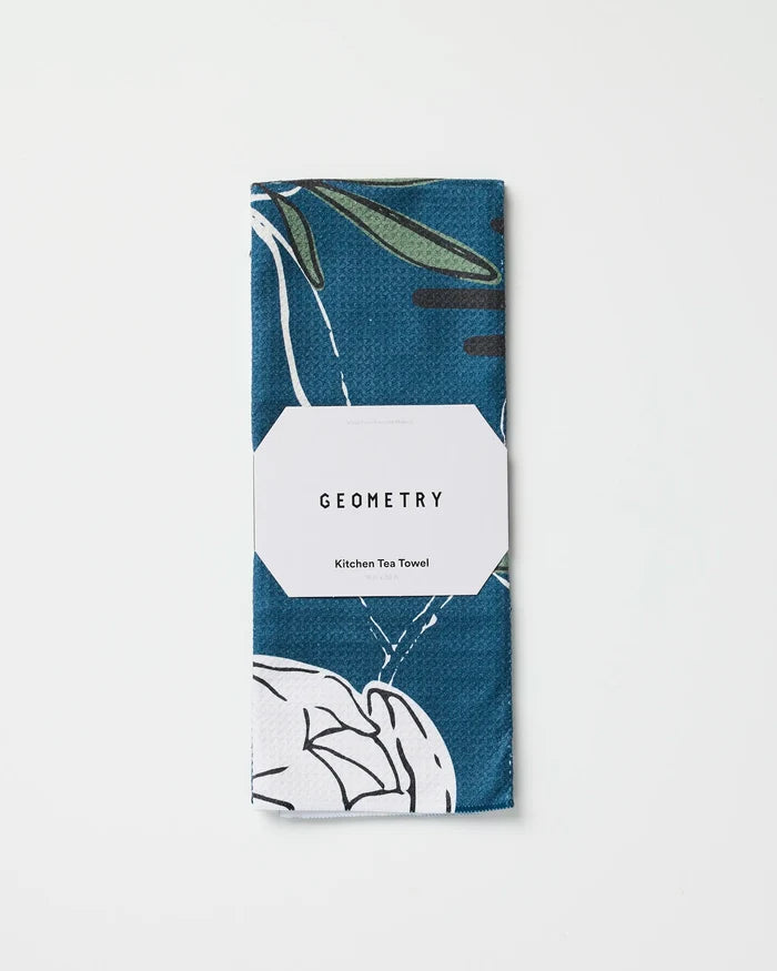 A folded blue and white recycled tea towel with a geometric pattern, wrapped in a white label that reads Ashley Celena Blooming Possibilities, displayed on a plain white background.