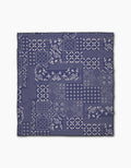 The Geometry Blossoming Bandanna Blue beach blanket features a navy blue and white patchwork pattern of floral and geometric designs in a quilt-like layout, made from quick-drying recycled materials, displayed on a white background.