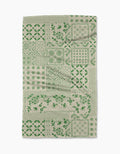The Blossoming Bandanna Green tea towel by Geometry features a patchwork of green floral and geometric designs in squares and rectangles on an off-white background.