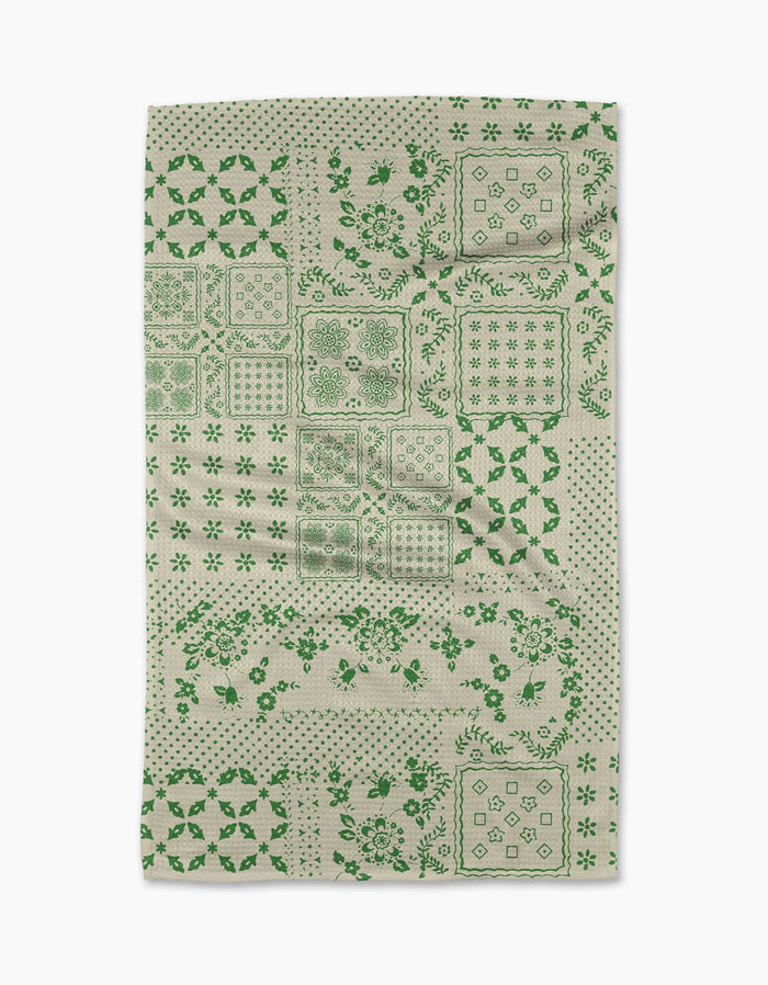 The Blossoming Bandanna Green tea towel by Geometry features a patchwork of green floral and geometric designs in squares and rectangles on an off-white background.