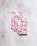 Six "Blossoming Love" GEOMETRY reusable towels, in pastel abstract floral patterns of pink, purple, orange, and green, are fanned out on white marble—offering an eco-friendly alternative to Not Paper Towels.