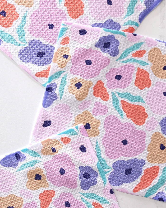 The GEOMETRY Blossoming Love set includes three super-absorbent dishtowels with a waffle-textured surface and a pastel floral print in purple, orange, pink, and blue on a white background.
