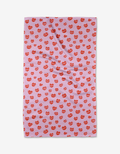 The Kayla Ann Blowing Kisses tea towel is pink and rectangular, featuring a red lips pattern. Made from recycled materials, it’s shown laid flat with slight wrinkles visible.