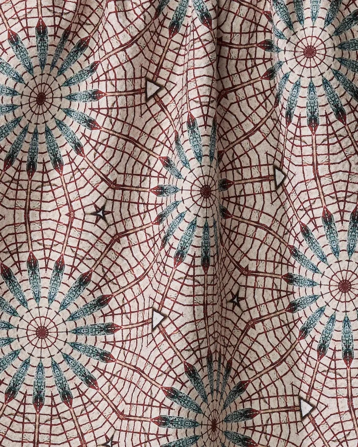 A close-up of the Blue Aster Foxtrot kitchen towel by Katherine Berkeley, made from recycled materials with red and blue circular, web-like patterns on a light beige background. Slight wrinkles add shadows and texture.