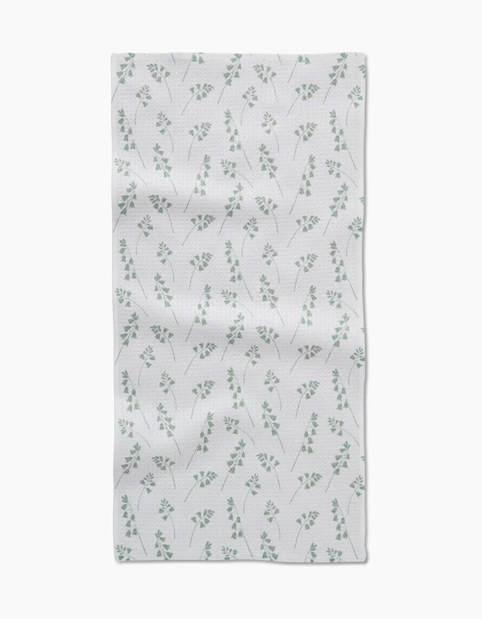 The Linda Fox Blue Bells Green Bar Towel features a Geoweave fabric with a subtle pattern of small green leaves and branches, evenly spaced on a white background, and a slight wrinkled texture for added charm.