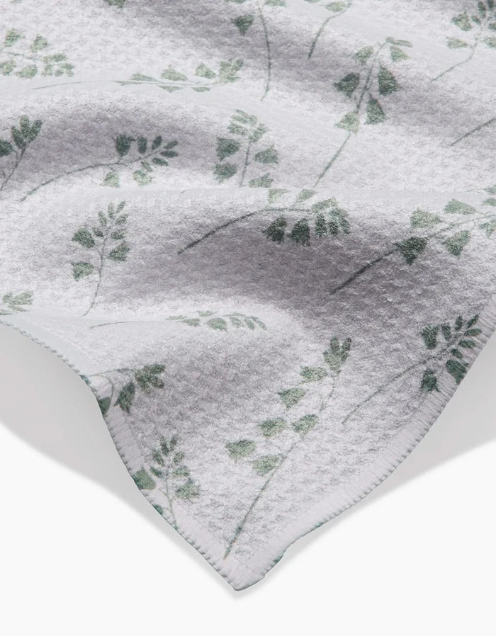 A close-up of the Linda Fox Blue Bells Green Geoweave bar towel in white, featuring a subtle green leafy branch pattern and a visible, neatly stitched hem.