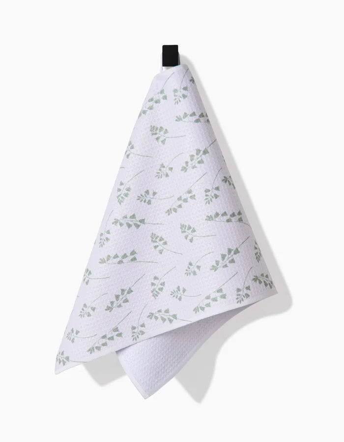 The Linda Fox Blue Bells Green Bar Towel, made from Geoweave fabric and featuring a subtle green leaf pattern, hangs from a black loop against a plain white background.
