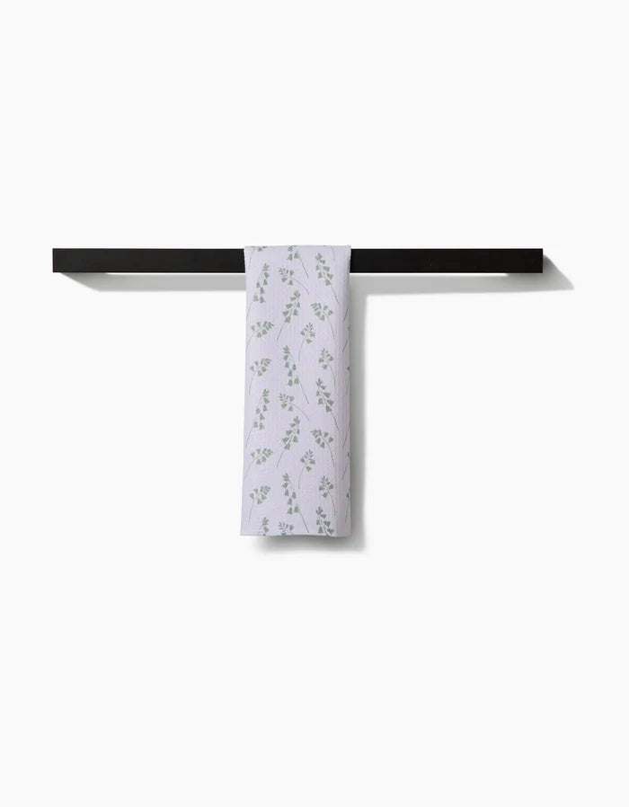 The Linda Fox Blue Bells Green bar towel, featuring a subtle green leaf pattern and crafted from Geoweave fabric, is draped over a black towel bar against a plain white background.