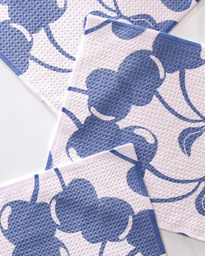 Three Blue Cherry Dreams cloths by Geometry lie overlapping on a white surface, each featuring blue abstract flowers and curving stems. Made from recycled materials, these dishcloths offer optimal absorbency and stylish charm.