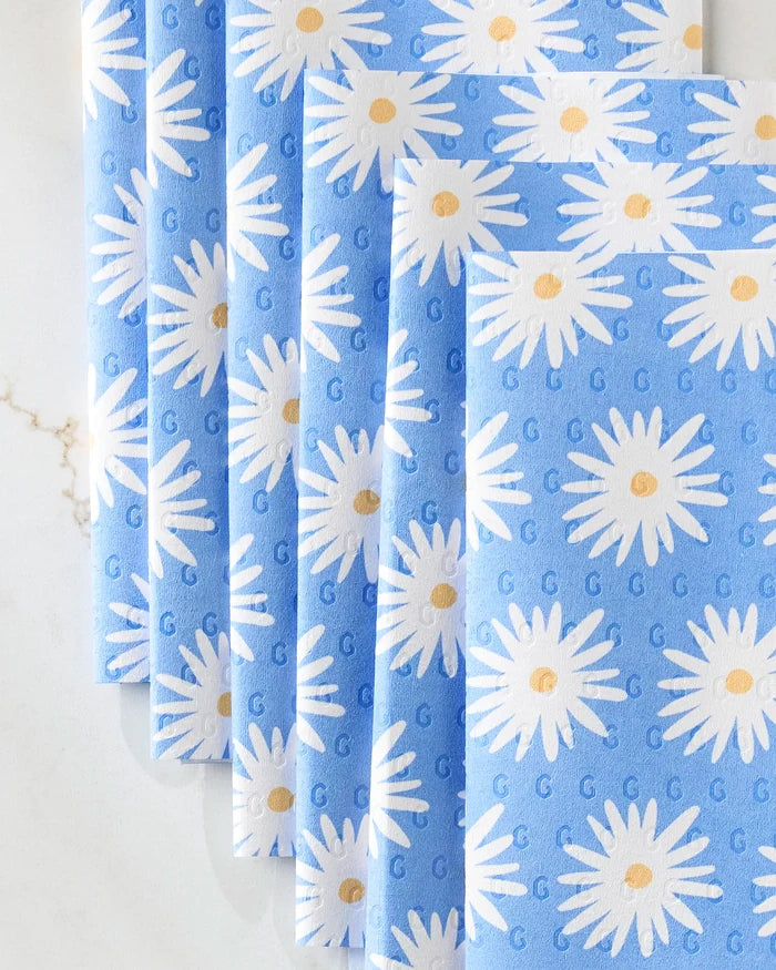 Four "Blue Daisies" reusable paper towels by Megan Roy, featuring blue fabric with white daisies and yellow centers, are arranged in an overlapping fan on a light marbled surface.