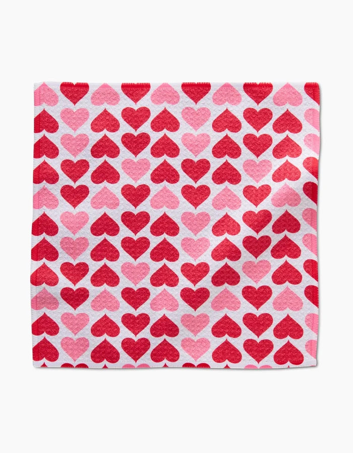 The Blushing Hearts cloth by Danelys Sidron is made from recycled materials and showcases a repeating pattern of red and pink hearts in neat rows on a white background.