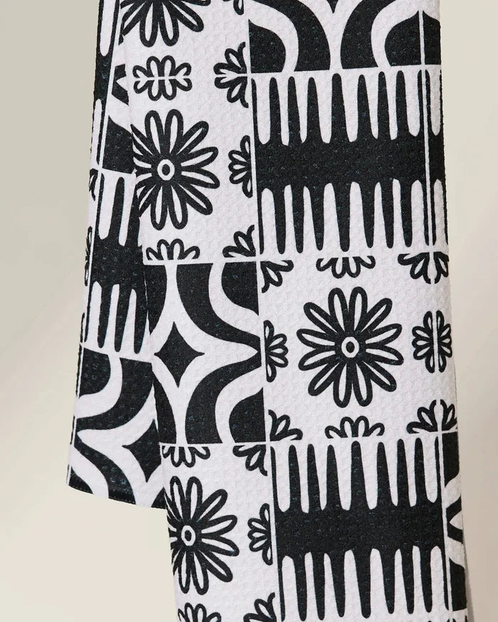 The GEOMETRY Bohemian Mosaic is a quick-drying towel showcasing black and white geometric and floral motifs—daisies, diamonds, and abstract shapes—in a repeating grid design.