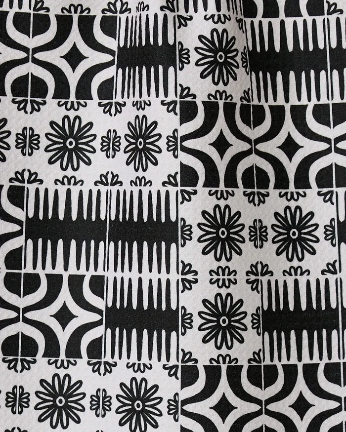 Bohemian Mosaic by GEOMETRY features black and white tiles with alternating geometric and floral patterns, including starbursts, lines, and curves. Crafted from recycled materials, these designs repeat in a grid for a bold look.