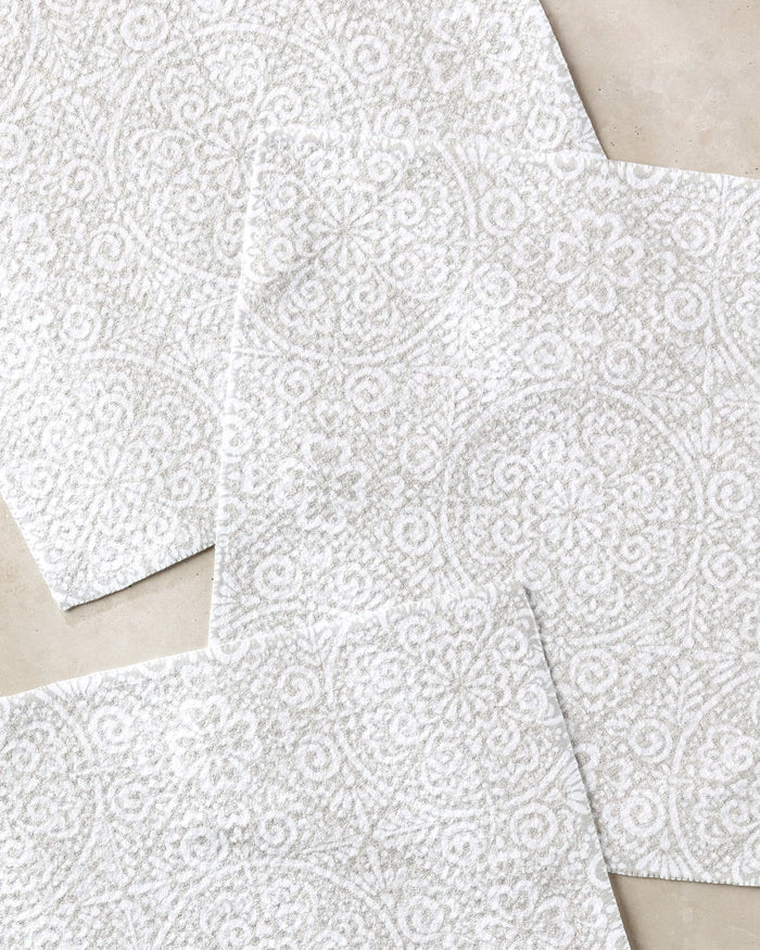 Three Boho Medallion tiles by Kris Ruff—white with intricate floral and circular textures, made from recycled materials—are overlapped on a light beige surface in a layered arrangement.