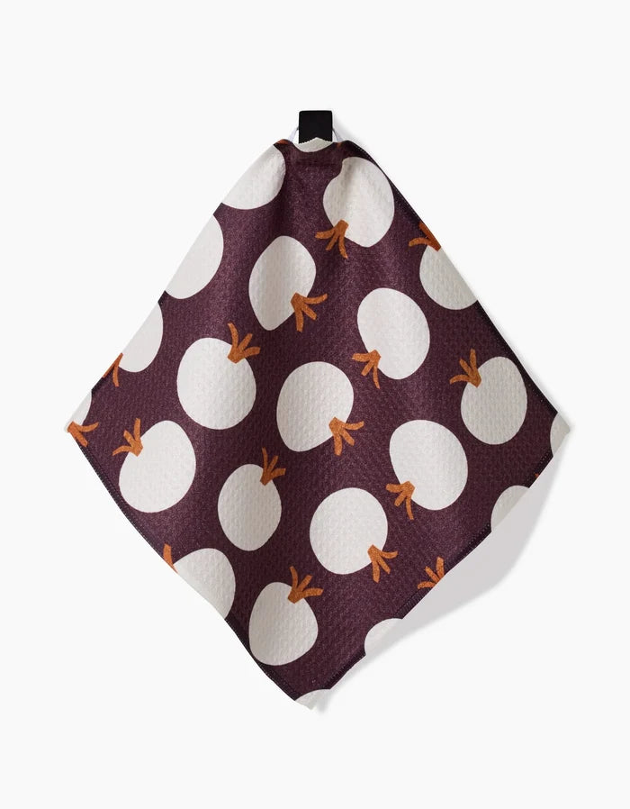 The Bold Fall dish towel by Lizzie Clark features a dark purple background with large white circles and orange stems like stylized pumpkins. Fast-drying and square, it includes a small black hanging loop at the top.
