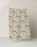 The Bonfire Nights tea towel by Geometry features brown, hand-drawn style musical instruments, books, and abstract shapes on beige. Made from recycled materials, it hangs against a light background.