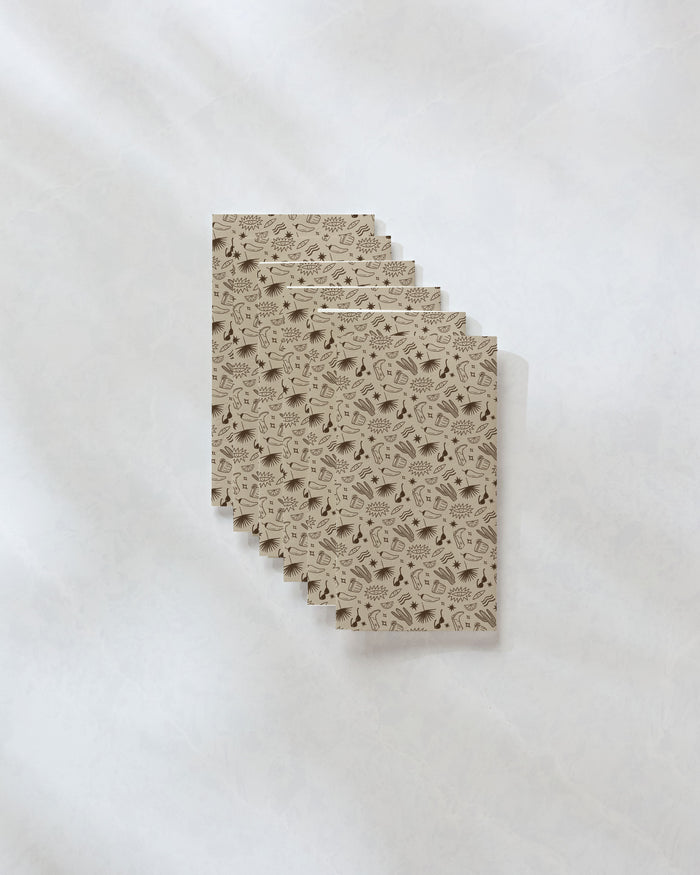 Six "Bonfire Nights" notebooks by Geometry, featuring a black nature-inspired pattern on brown kraft covers made from eco-friendly paper, are fanned out neatly on a light gray marbled surface.