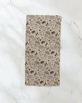 The Bonfire Nights bar towel by Geometry, featuring brown comic-style guitars, microphones, notes, stars, and sound bursts on beige fabric, is displayed on a white marble surface.