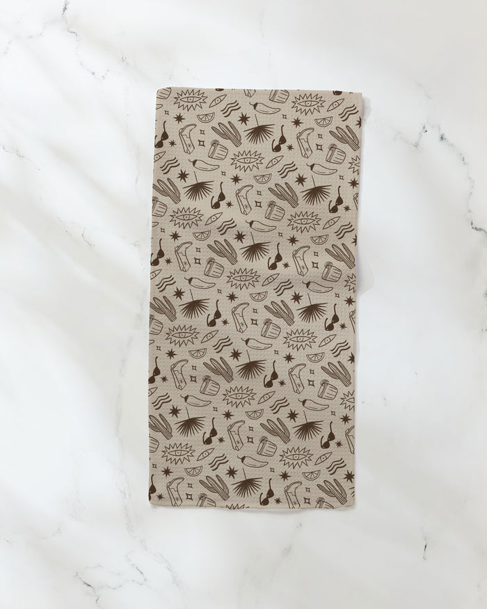 The Bonfire Nights bar towel by Geometry, featuring brown comic-style guitars, microphones, notes, stars, and sound bursts on beige fabric, is displayed on a white marble surface.