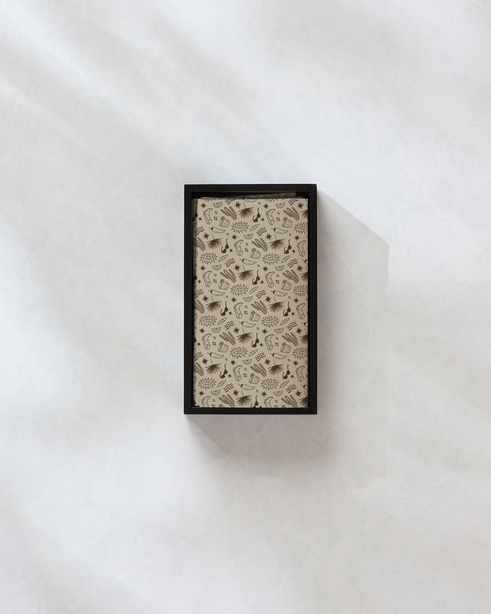 A closed rectangular box of Geometry’s Bonfire Nights eco-friendly paper towels with a light brown lid featuring small, dark brown icons sits on a textured surface with soft shadows.