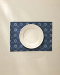 A white ceramic plate is centered on the Geometry Bonnie Indigo machine washable placemat, featuring a light floral pattern, atop a cream-colored tablecloth.
