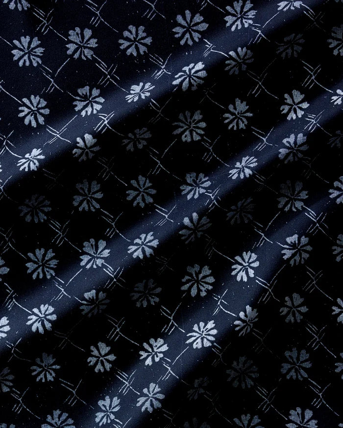 Bonnie Indigo reusable napkins by Geometry feature a dark fabric with a repeating white floral and geometric pattern, highlighted by diagonal light and shadow across the surface.
