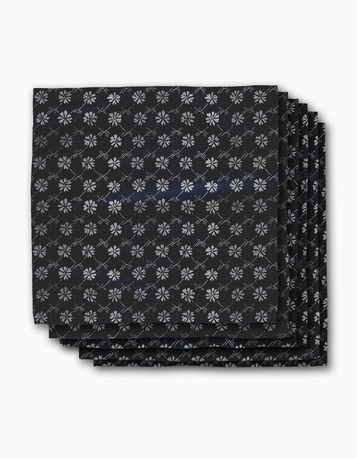 Four neatly stacked Bonnie Indigo napkins by Geometry, featuring a repeating white snowflake-like pattern on black, displayed against a plain white background.