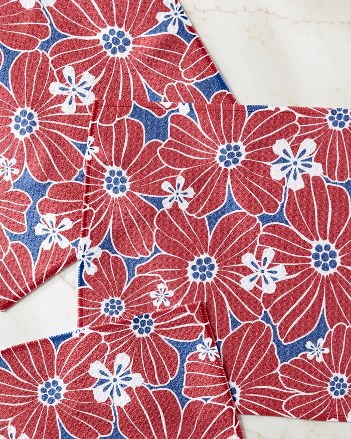 Botanical Blush napkins by Ashley Celena, with red and white florals on blue, overlap elegantly on marble—adding vibrant decor to your kitchen. Ideal for use in colorful dishcloth sets or as absorbent dishcloths.